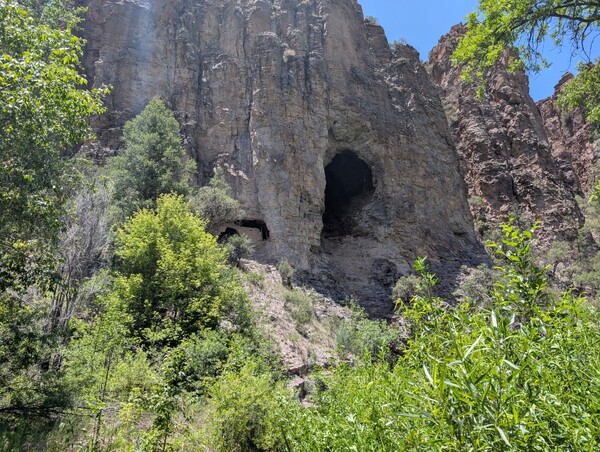 Two natural caves in a canyon wall, the left one has ruins of a cliff dwelling in it
